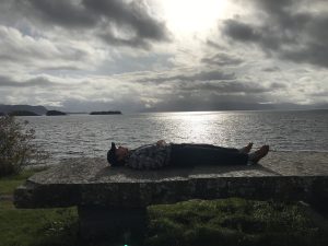 Person liggende på stein bord foran fjord